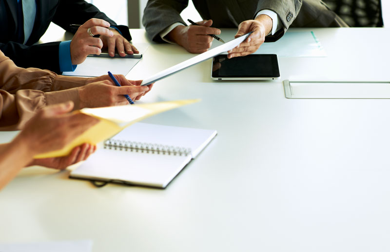 Fyra personers händer syns tillsammans med surfplattor, pennor och block